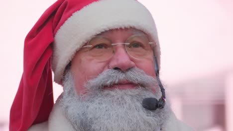 closeup of the face of an old grayhaired santa with a beard on a blurred background closeup of the face of an old grayhaired santa with a beard on a blurred background speaking into a microphone american santa claus talking to camera wishing merry christmas