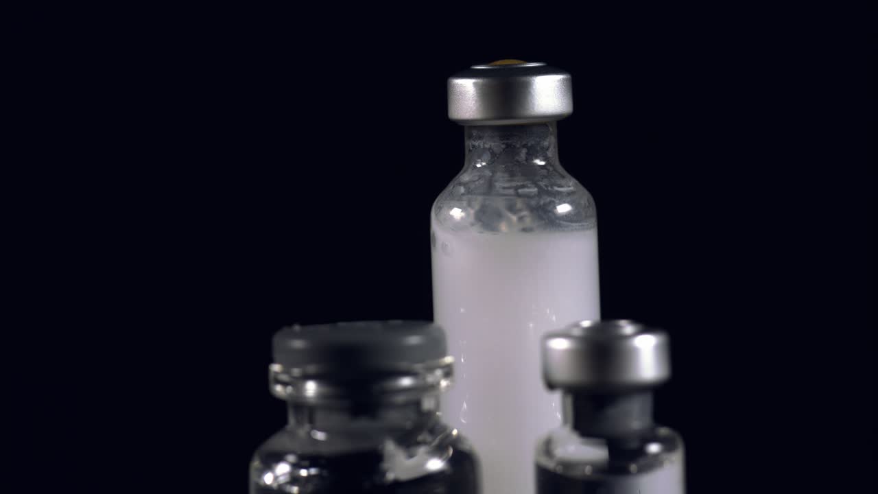 주사기로 주입할 준비가 된 거품이 나는 흰색 액체가 있는 앰플 - 검은색 배경으로 고정적으로 격리됨