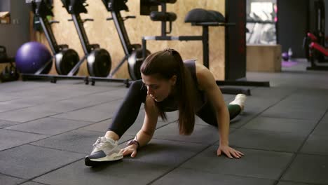 Attractive-brunette-female-in-her-20's-stretching-out-in-the-gym,-preparing-leg-muscles-to-do-the-splits.
