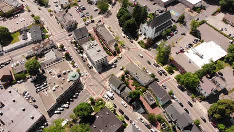 a daytime birds-eye drone view of a suburban downtown traffic grid among the buildings and shops, cars and other vehicles driving on the roadway