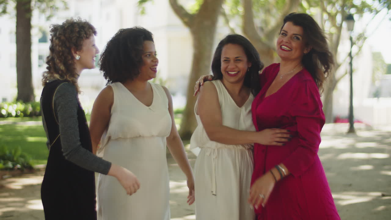 amigos abrazándose con novias en el parque después de la ceremonia de boda y mirando la cámara