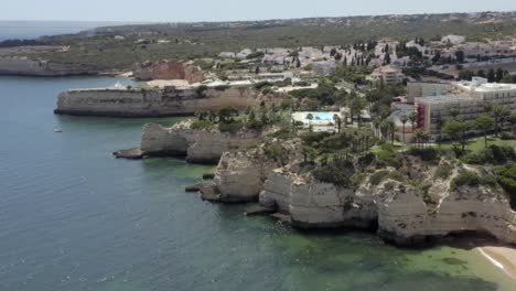 drone flies high over epic coastal cliffs with luxury hotels and buildings on top during a beautiful day, aerial