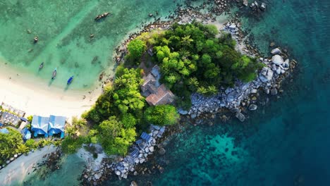 aerial view flight of a hut on a tropical sole peninsula with turquoise water and lush green vegetation