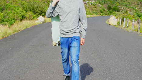 side view of cool young caucasian man with skateboard walking at countryside road 4k