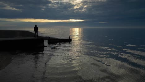 slow motion flying towards man silhouetted at jetty end at sunset on fleetwood beach lancashire uk