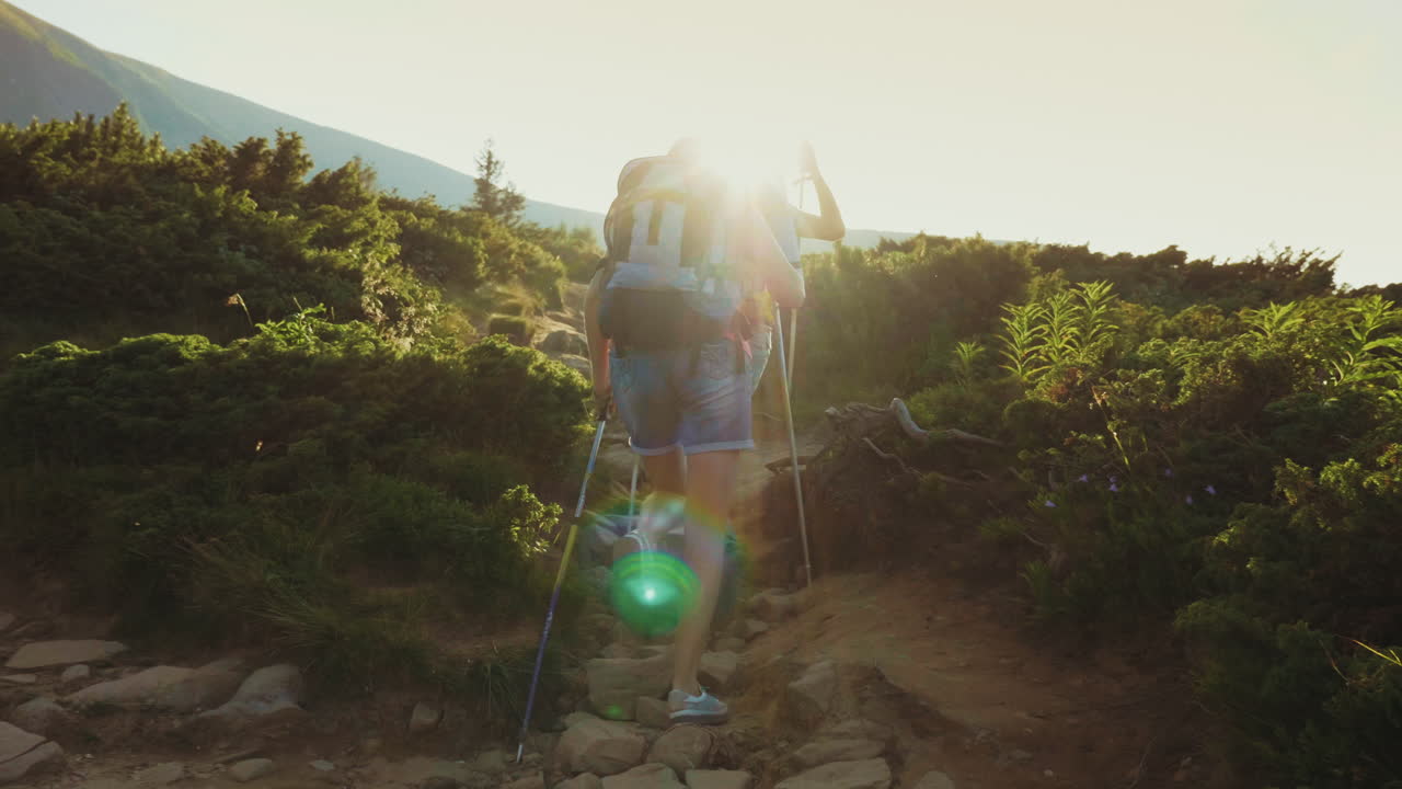 una turista con una mochila con bastones de trekking sube por el camino de la montaña en los rayos del s