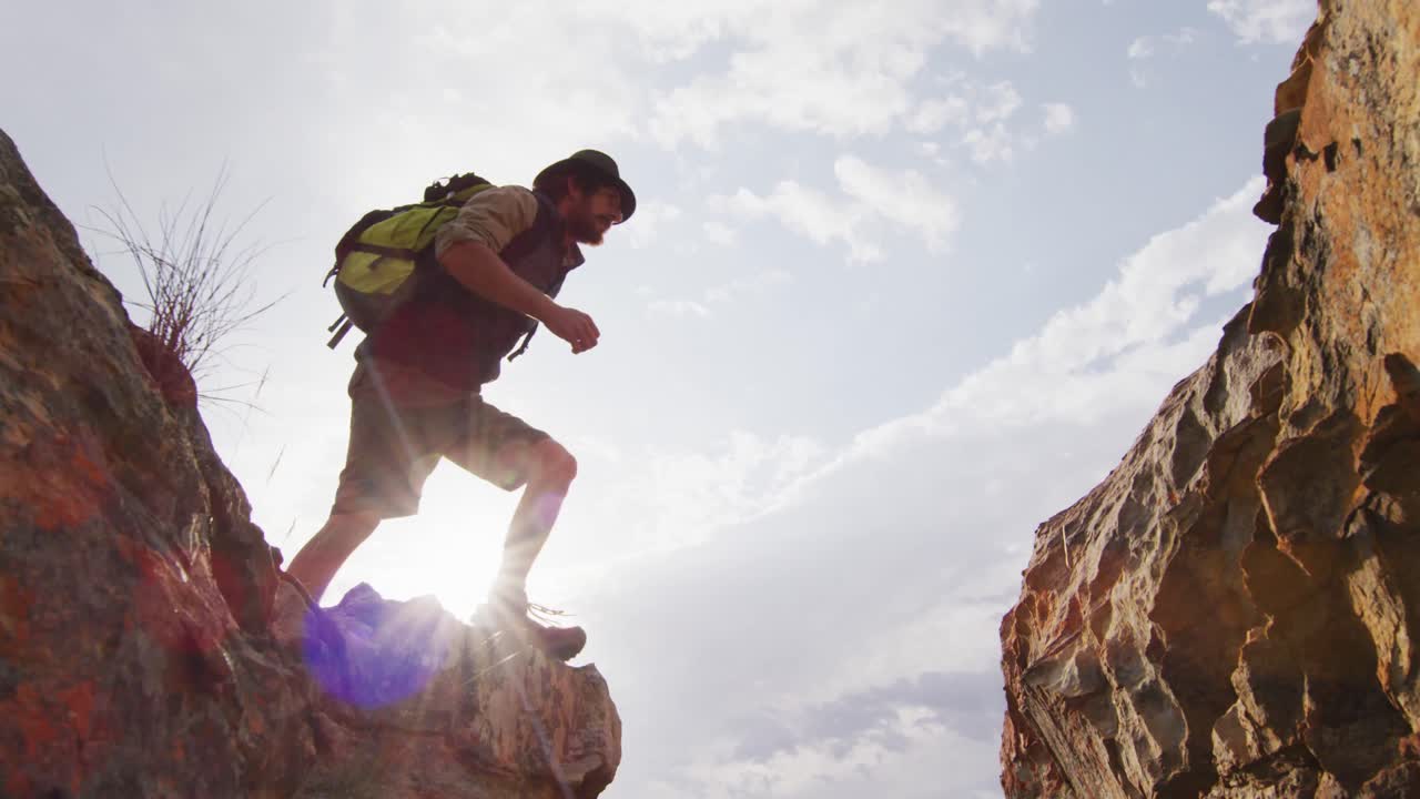 sobreviviente caucásico barbudo con mochila saltando a través de un barranco de montaña rocosa en el desierto