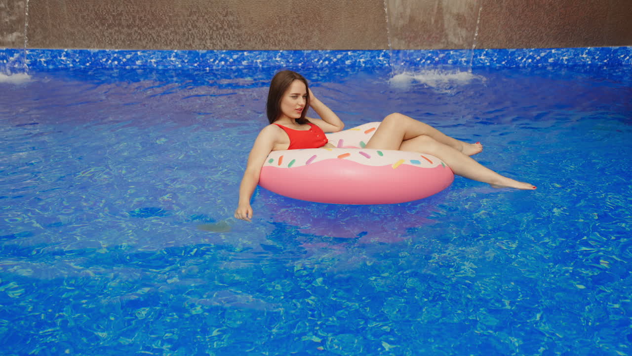Long-haired girl in a swimming suit like a bagel enjoying sun. Young lady spending time in a pool outdoors.