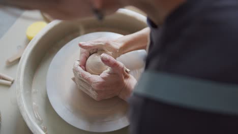 female potter shapes piece of clay on the pottery wheel.