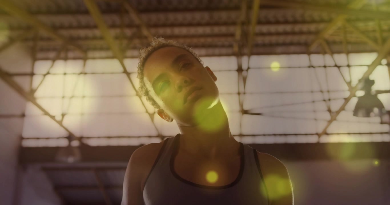 Vídeo vertical: Mulher de regata se inclinando e aquecendo na academia sob um reflexo de luz com feixes