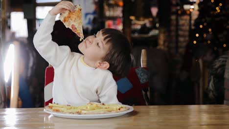 el niño se divierte mientras come pizza con salchichas, queso, maíz y papas fritas en el restaurante