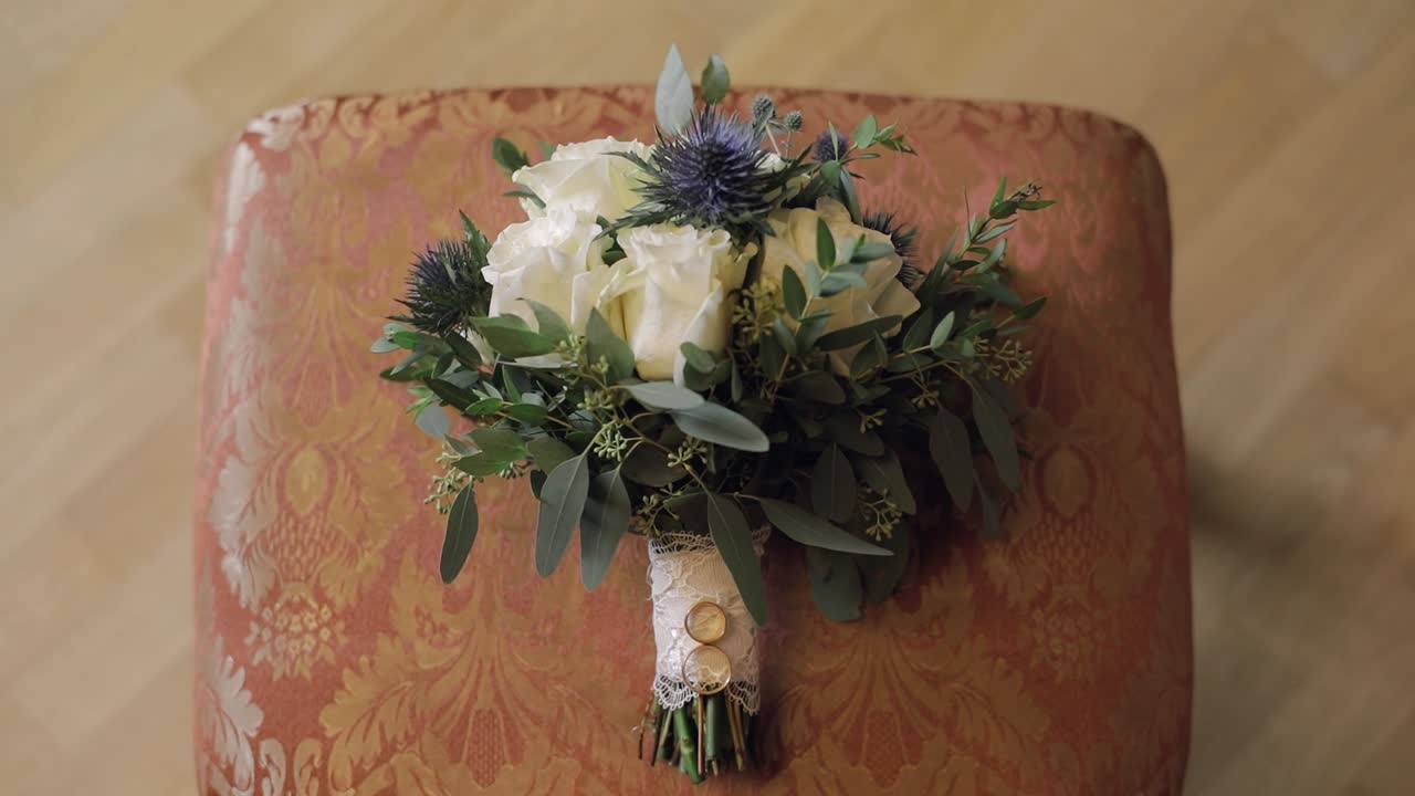 Wedding rings lie on a beautiful wedding bouquet which lays on the chair
