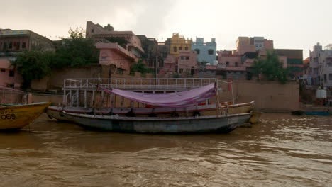 Cinematográfica-Cámara-Lenta-Varanasi-India-Crucero-Por-El-Río-Ganges-Barcos-Canal-Estado-Del-Norte-Gran-Reunión-En-La-Orilla-Antigua-Ciudad-Santa-Provincia-De-Ghat-Pradesh-Paisaje-Gris-Tarde-Nublada-Fangosa-Marrón-Izquierda