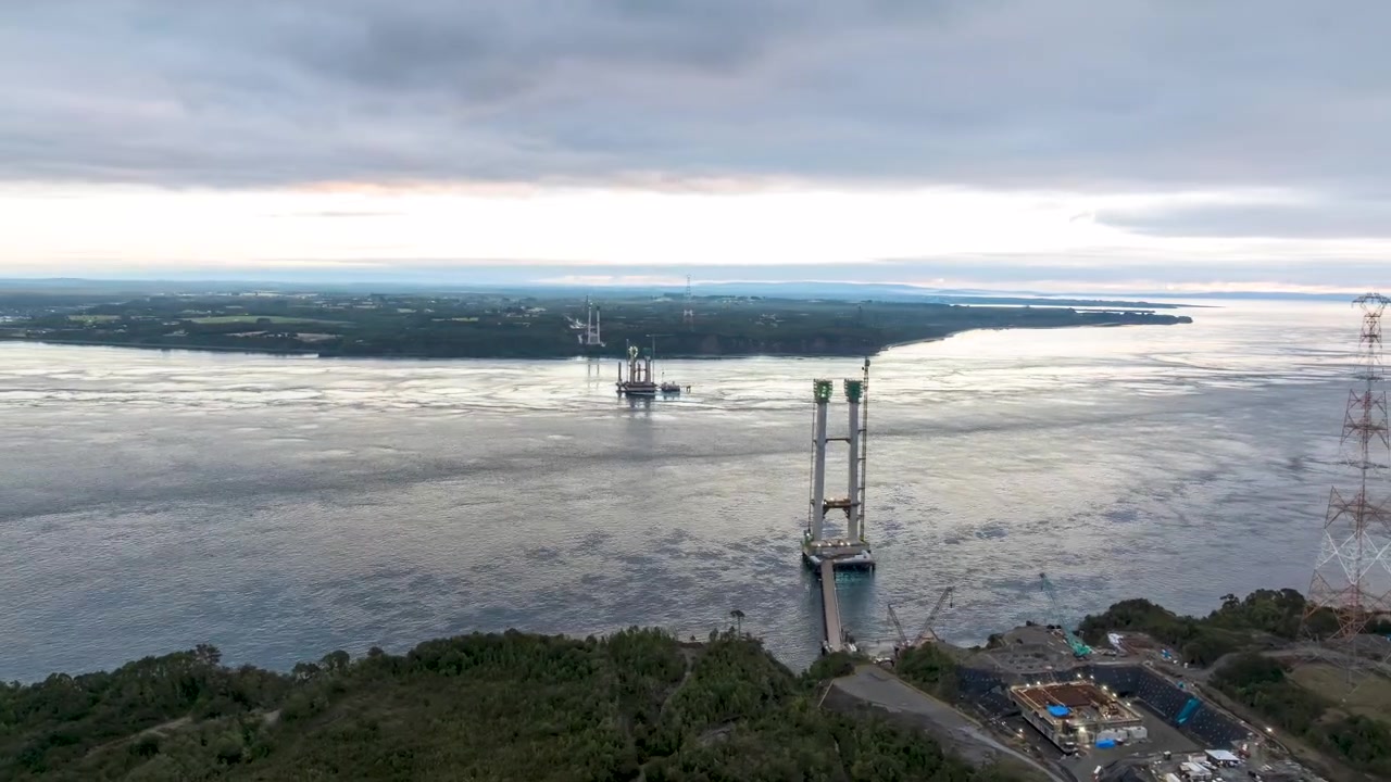 Chacao Channel stretches beneath dramatic moving clouds in this aerial hyperlapse. Bridge towers and construction site emerge as the camera reveals the scale of this engineering megaproject.
