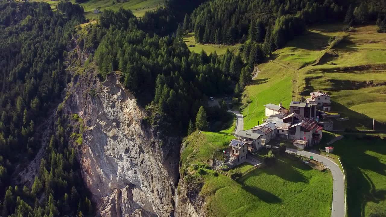 바위 벽 가장자리에 있는 작은 고산 마을, 푸른 풀 필드, 소나무 숲, 공중 촬영