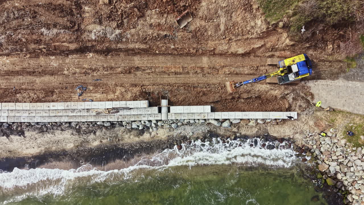 Lavori di Costruzione sulla Costa con Macchinari che Posano Blocchi e Operai che Assistono Vicino all'Acqua