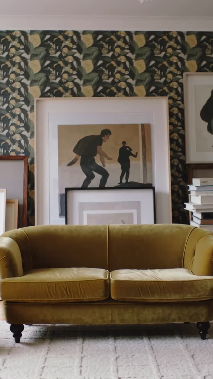 Video verticale: Carrellata della telecamera che rivela un divano verde oliva in studio, mostrando opere d'arte e libri appoggiati.