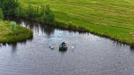 a high-angle aerial shot shows a young couple in a small rowboat enjoying a peaceful and romantic summer day on a calm lake in the latvian countryside