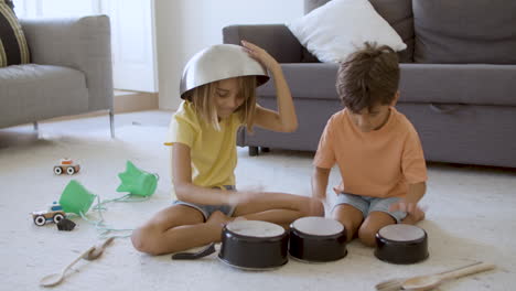 chica feliz con un cuenco en la cabeza jugando con su hermano en casa