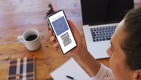 mujer en el escritorio con un teléfono inteligente con certificado de vacunación contra la covid, bandera de la ue y código qr en la pantalla