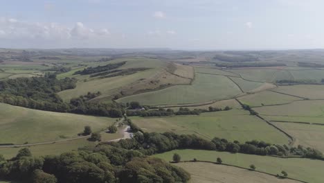 Wide-aerial-shot-tracking-across-the-fields-surrounded-by-Chesil-Beach-and-the-Village-of-Abbotsbury,-Dorset