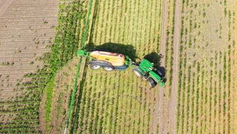 Colorful Top down aerial of green tractor spraying crops in diagonal lines across field