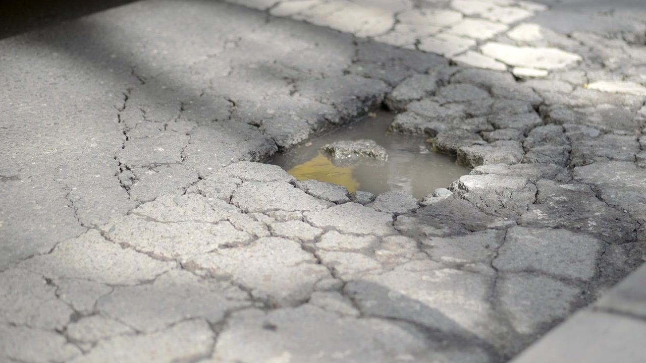 Pneumatico dell'auto che schizza acqua da una buca su una strada danneggiata