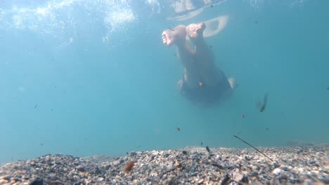 Man-elegantly-swimming-past-camera-sitting-on-lake-bottom---Static-underwater-clip-with-male-passing-close-to-camera---Bright-sunrays-and-reflections-from-surface---Glacial-lake-Lovatnet-Norway