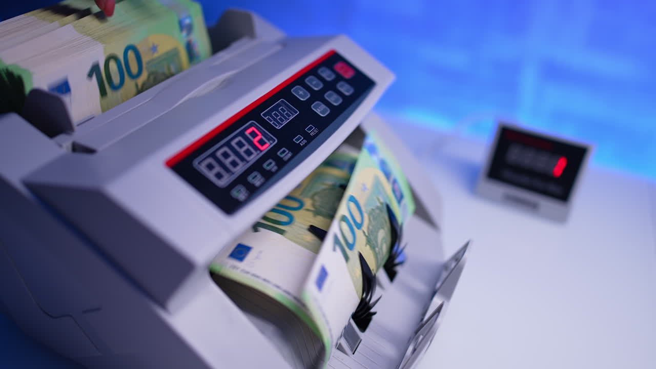 Female hand puts a thick stack of one hundred bills into the cash counting machine. Bank equipment working. Close up. Blurred backdrop.