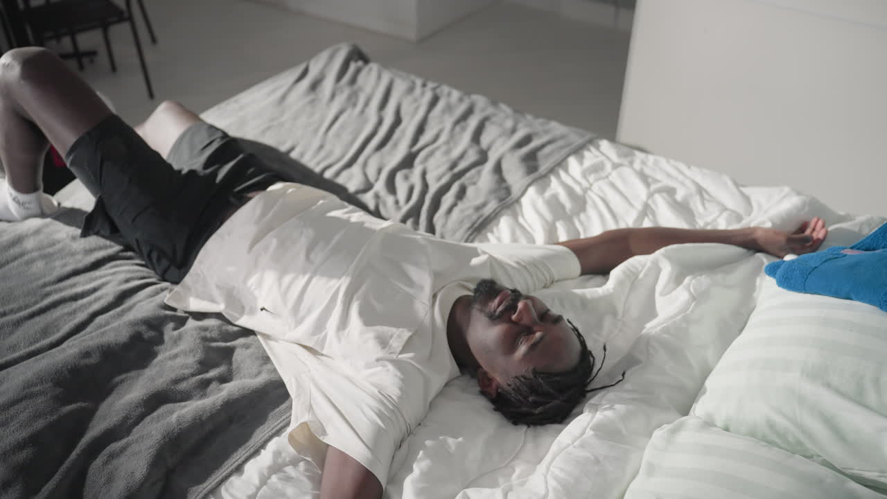 Person in white shirt vacuuming bedroom floor, modern interior, green curtains, bed with grey blanket and white pillows, soft natural light coming through window, cleaning, home care, tidy environment