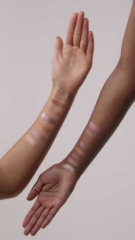 cerca de los brazos de dos mujeres con muestras coloridas de diferentes productos de maquillaje