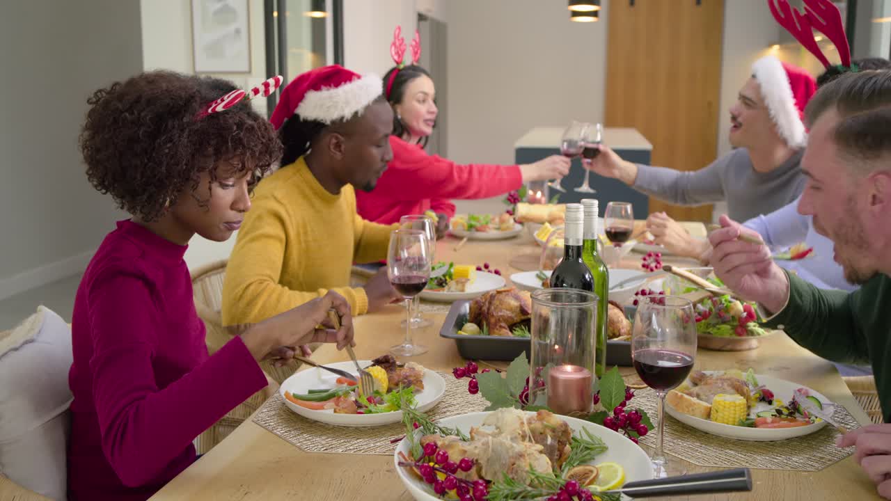 Diverse friends raising glasses during holiday meal, carving turkey, passing salad at dining table