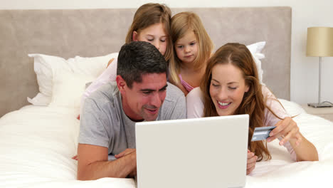 parents and daughters lying on bed shopping online with laptop