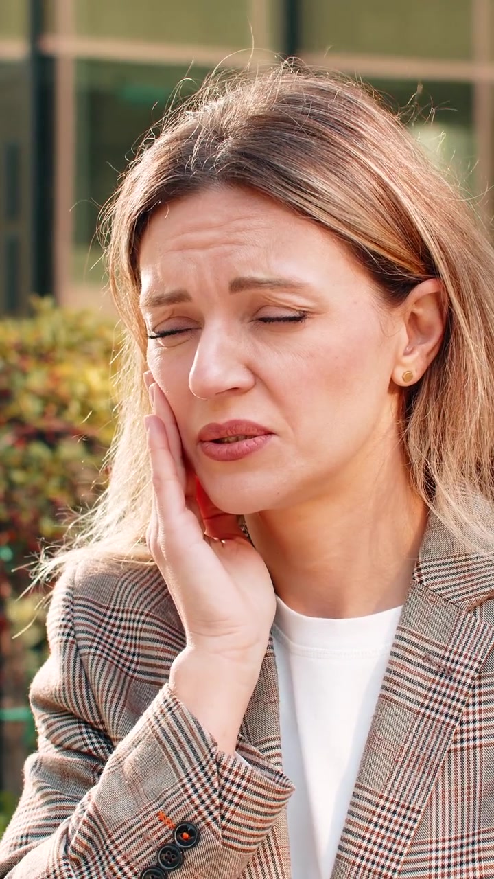 Young woman feeling tooth pain and discomfort on bench in city street during office break outdoors