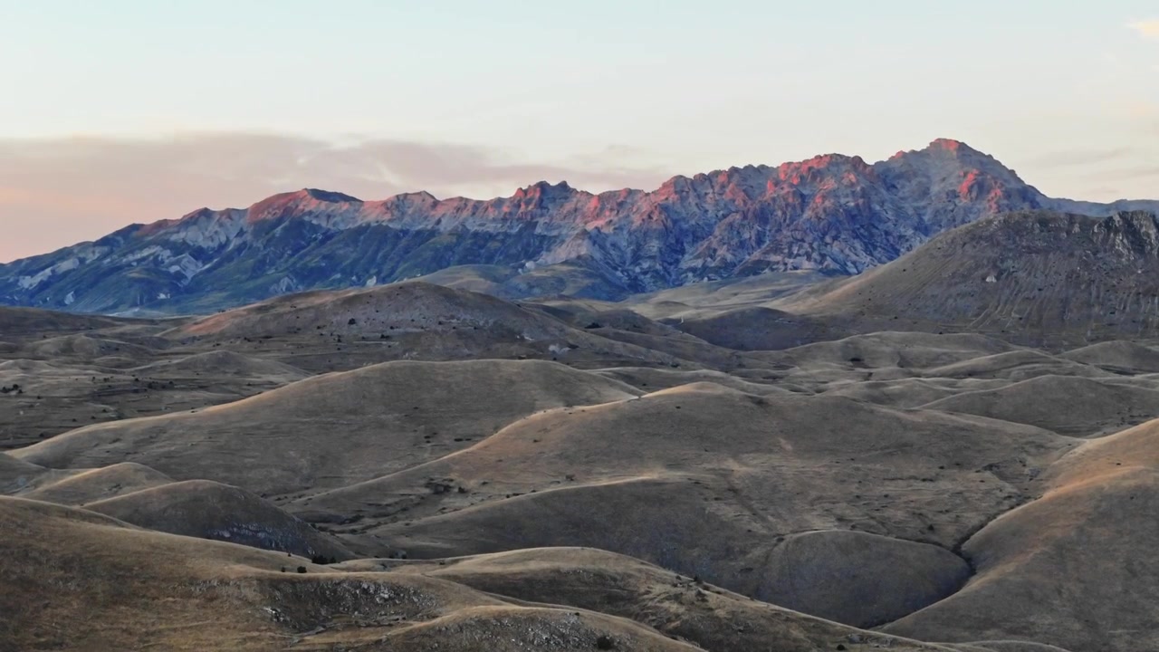 A wide shot of the Gran Sasso mountain range in Abruzzo, Italy, featuring rolling hills and rocky peaks illuminated by the warm light of a golden hour sunset