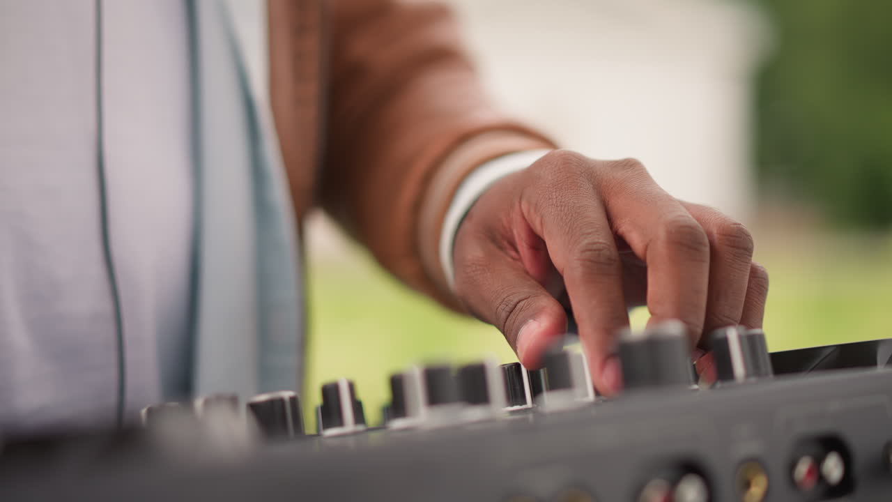 Mani che mettono a punto l'attrezzatura audio, musicista che manipola le manopole del mixer durante una sessione di pratica all'aperto, disc jockey che regola le impostazioni del mixer e testa i campioni audio durante una prova all'aperto.