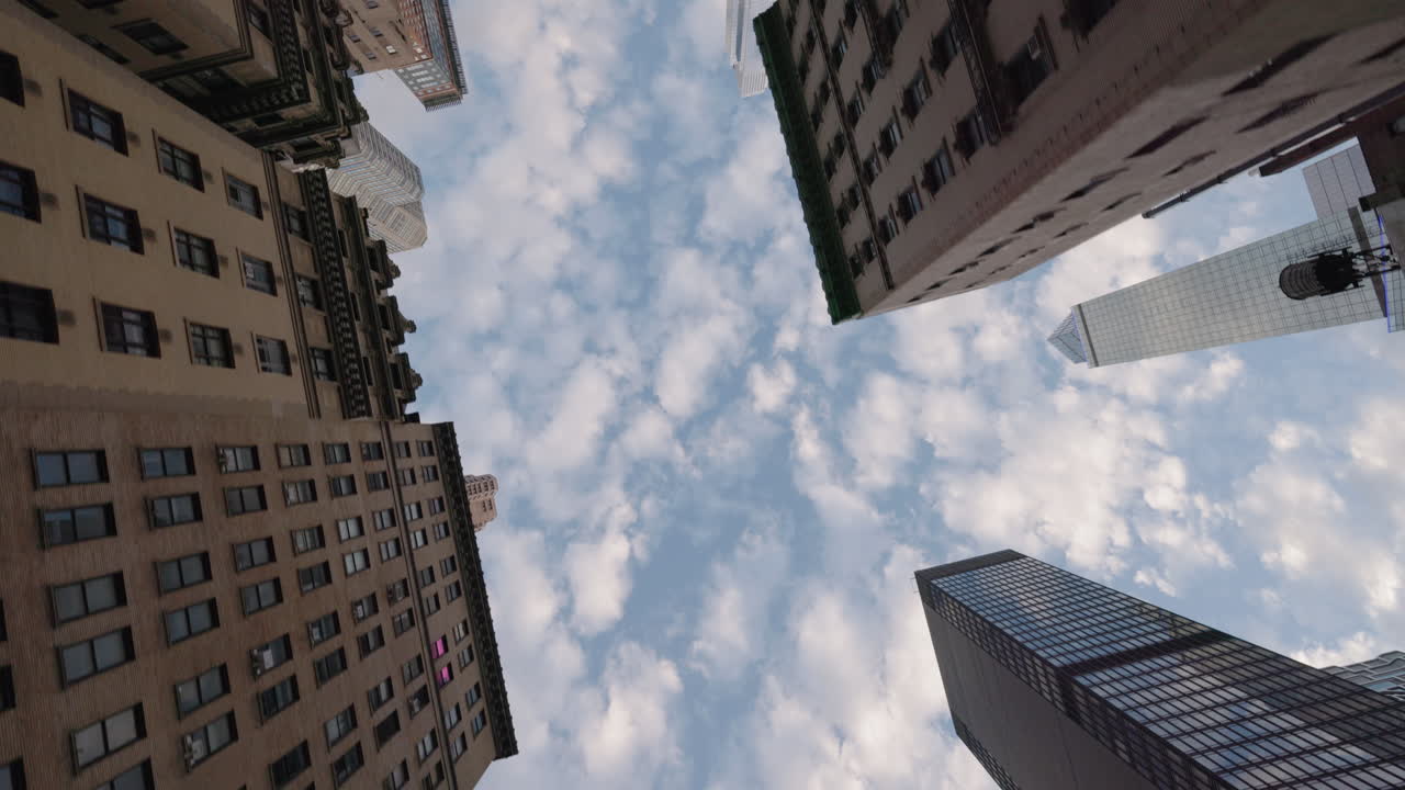 Vista em ângulo baixo de arranha-céus emoldurando o céu nublado em Manhattan, Nova York, com arquitetura urbana e uma perspectiva dramática da cidade.