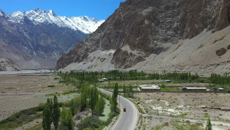 cinematic drone shot of passu cones in hunza pakistan, moving towards the tupopdan peak with a tuk tuk driving on karakoram highway, wide shot