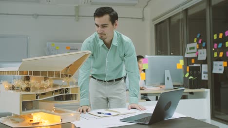 joven arquitecto caucásico confiado trabajando en un modelo arquitectónico en la oficina por la noche