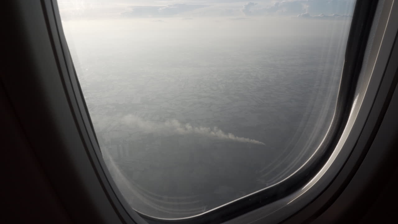 4K zoom out shot of huge agricultural fields in Asia with smoke from farm burning as seen from the window of a flying airplane