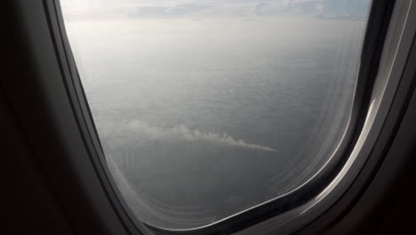 4k zoom out shot of huge agricultural fields in asia with smoke from farm burning as seen from the window of a flying airplane