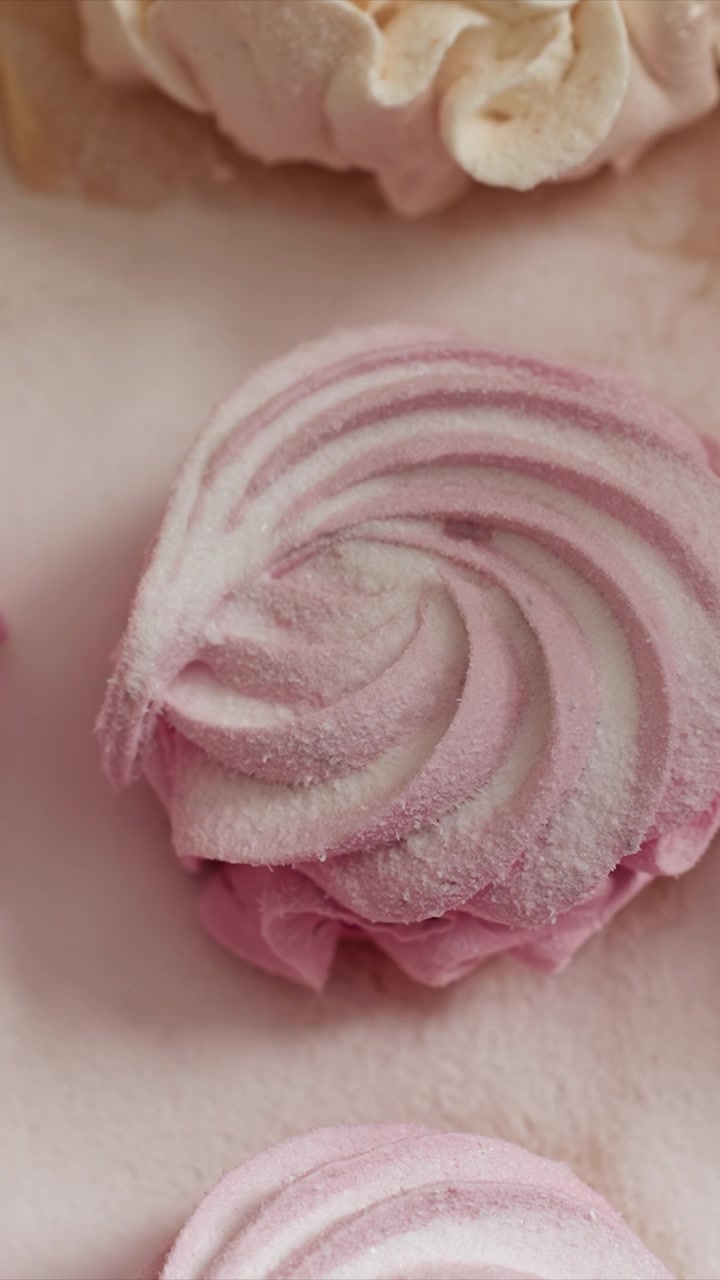 Primo piano di biscotti meringa rosa a spirale cosparsi. I dolci hanno una consistenza morbida e un motivo a spirale liscio. Lo sfondo rimane sfocato per enfatizzare la vista dettagliata.