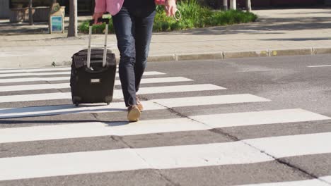 Low-section-of-man-with-trolley-bag-crossing-the-city-street