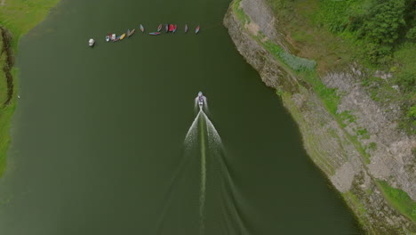 aerial view of a motorboat on a green lake with canoes and cliffs