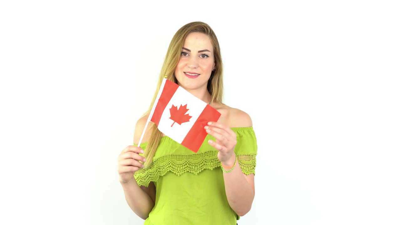 Mujer joven rubia ondeando la bandera de Canadá frente a un fondo blanco.