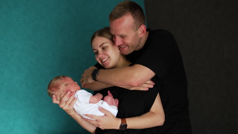 caucasian woman holding her newborn in front of her. husband embracing her from the back looking at baby with a happy smile.