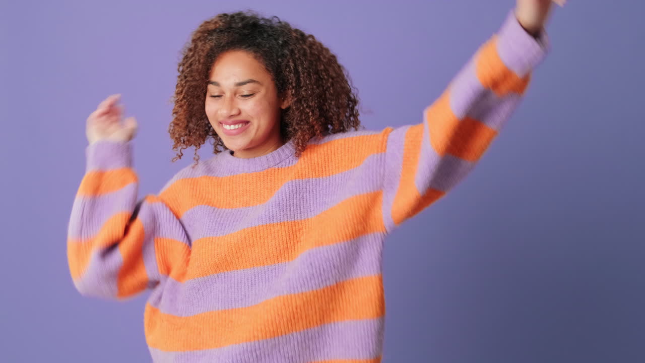 Jeune femme heureuse aux cheveux bouclés dansant joyeusement en studio