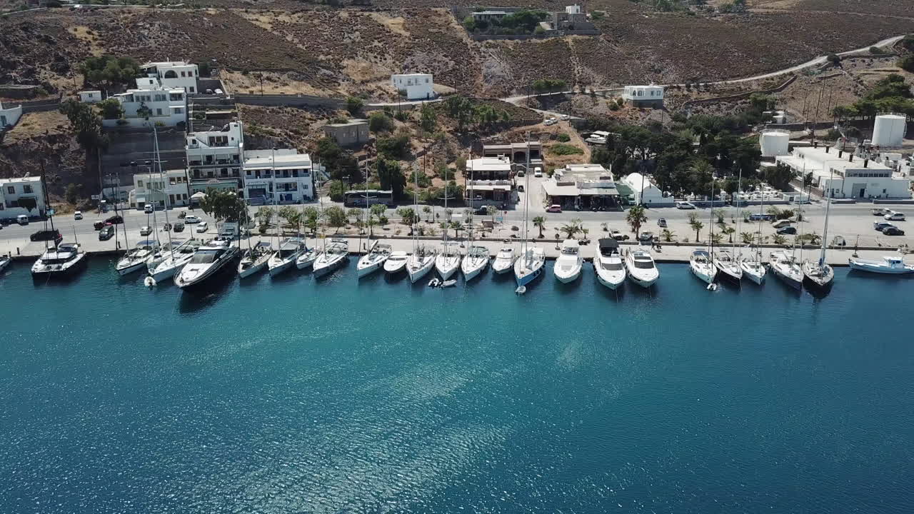 Greece, Patmos Island, Drone Footage of the harbor and town quay. Boats stern-to and the traffic of the cars along the seaside road.Aerial view of the Scala Town over the Marina,big yachts,sailboats