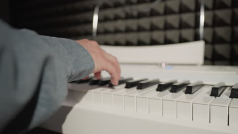 close-up shot of a hand wearing a blue sleeve playing a piano, with a detailed focus on the fingers and keys. the background features an acoustic wall