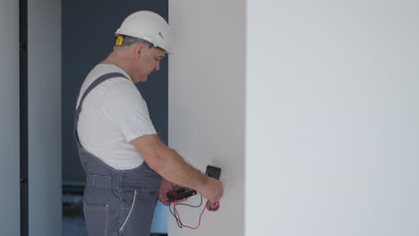 un hombre electricista con casco en el apartamento comprueba el trabajo de los enchufes después de la reparación